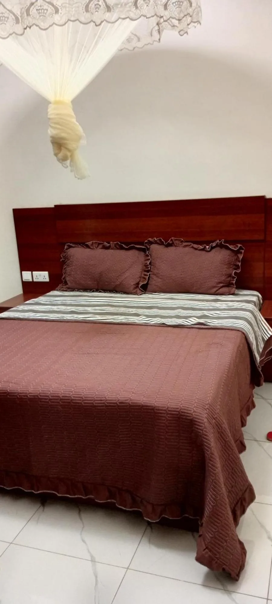Schlafzimmer im VENUS APARTMENT Kigali in Nyamata mit Doppelbett, Moskitonetz und Nachttischbeleuchtung.