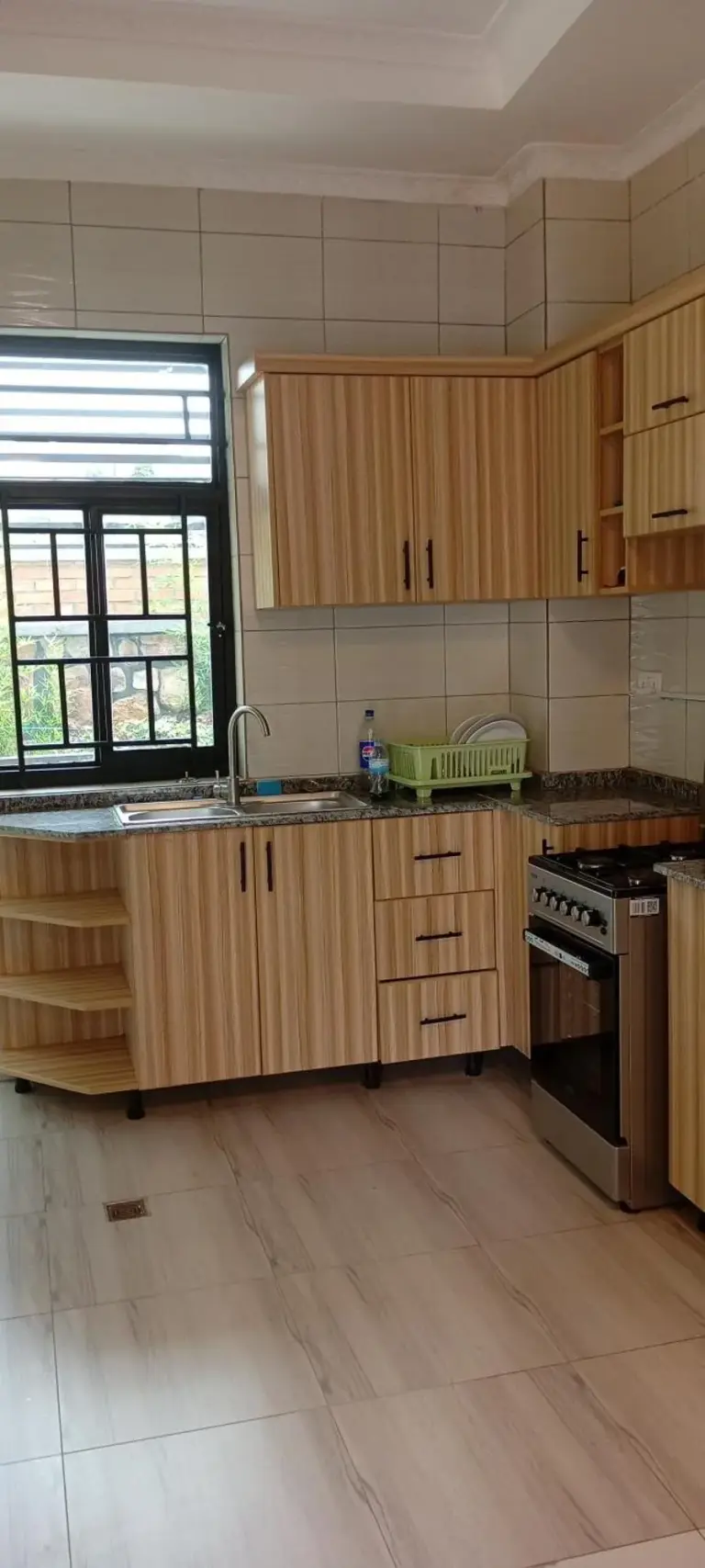 Voll ausgestattete Küche im VENUS APARTMENT Kigali in Nyamata mit Holzschränken, Herd, Spüle und Fenster.