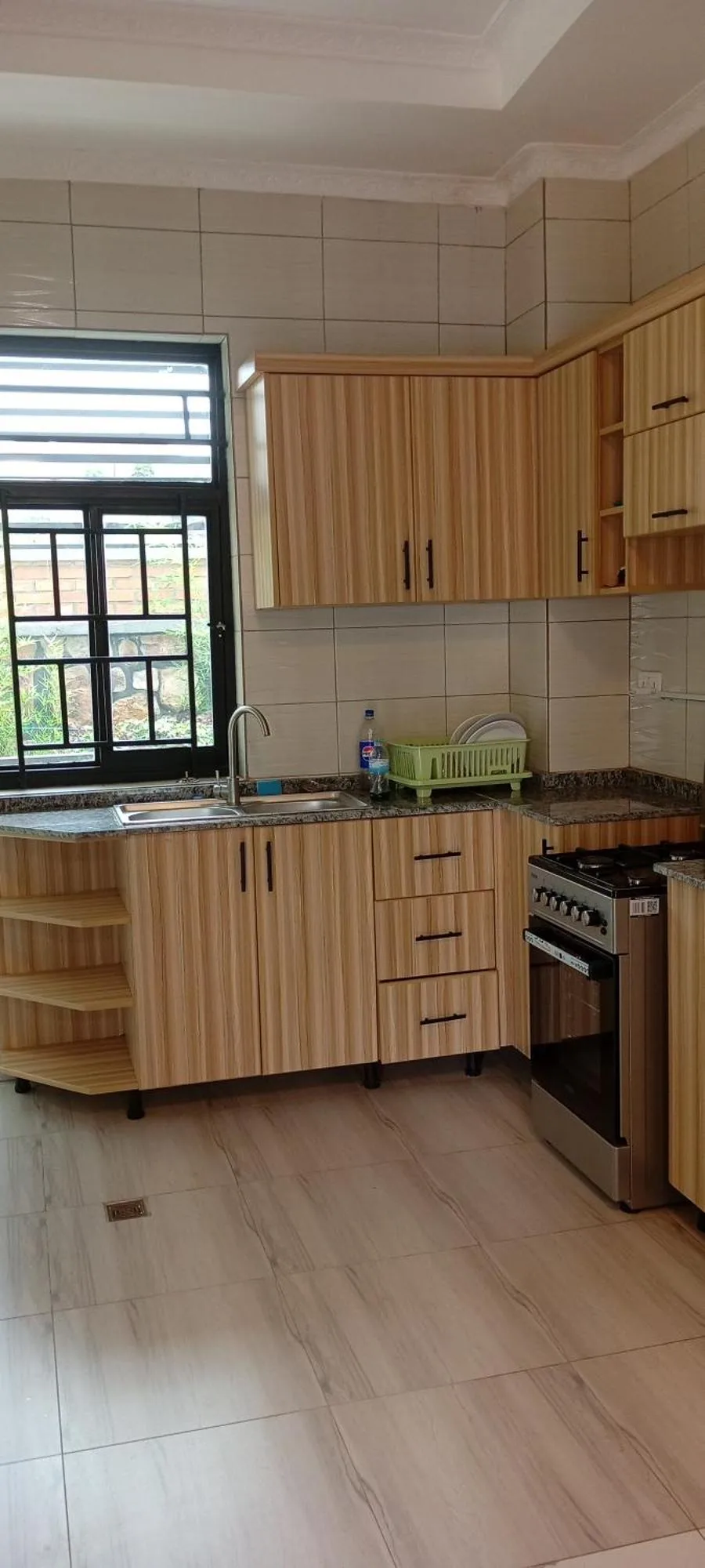 Voll ausgestattete Küche im VENUS APARTMENT Kigali in Nyamata mit Holzschränken, Herd, Spüle und Fenster.