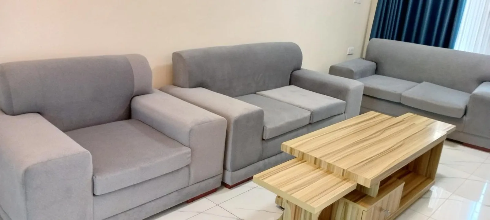 Lounge-Sitzbereich im VENUS APARTMENT Kigali in Nyamata mit grauen Sofas und einem Holzcouchtisch.