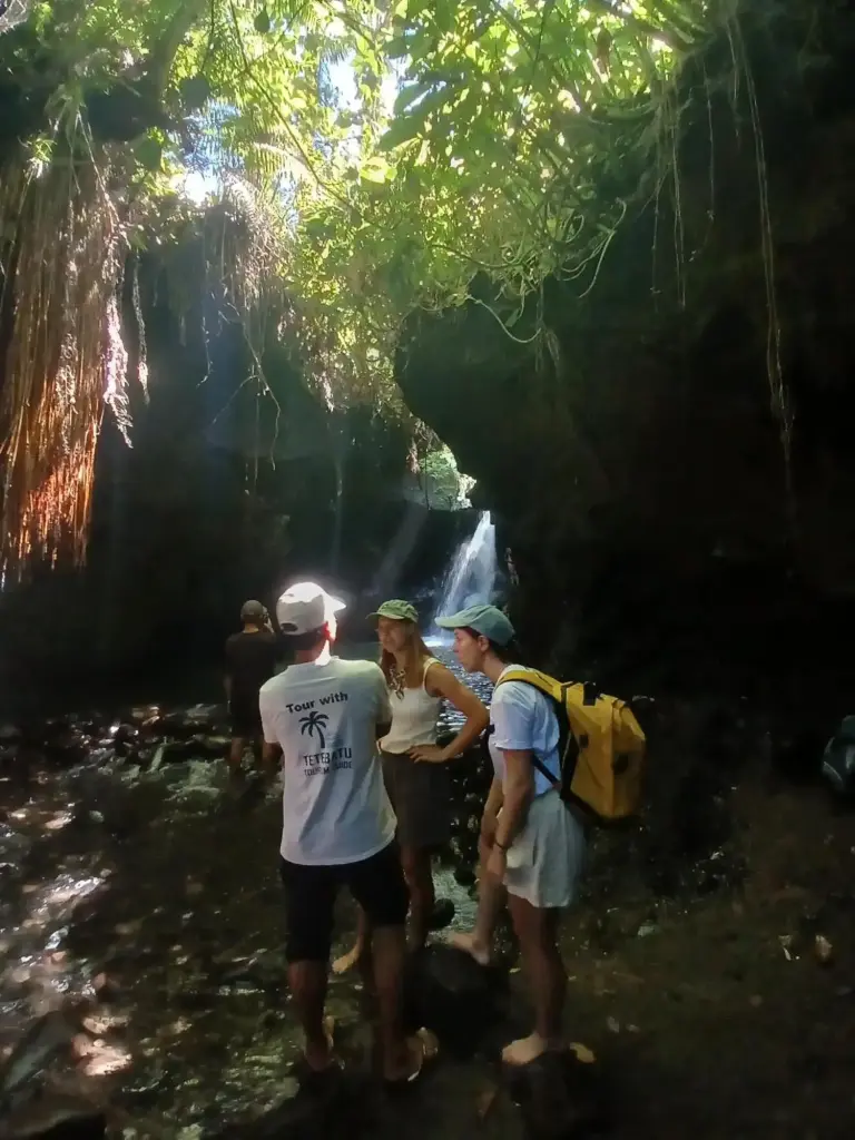 Viajeros de pie cerca de una cascada en un bosque frondoso durante una excursión desde Villa Puri Karang Bayan en Mataram.