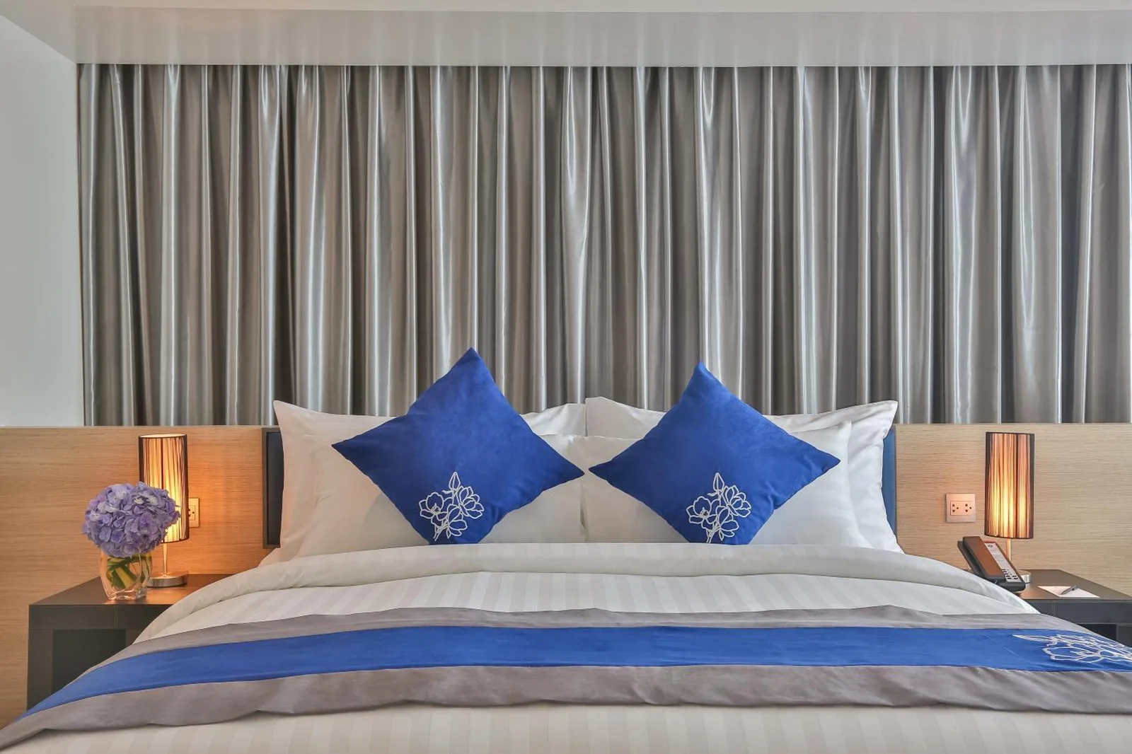 Vista en primer plano del dormitorio en Wintree City Resort Chiang Mai con la cama perfectamente hecha, cojines azules y cortinas.