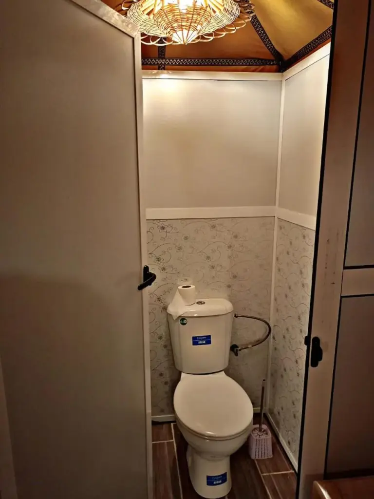 Compact private bathroom toilet inside Zahra Luxury Desert Camp in Merzouga with decorative lighting and tiled walls.