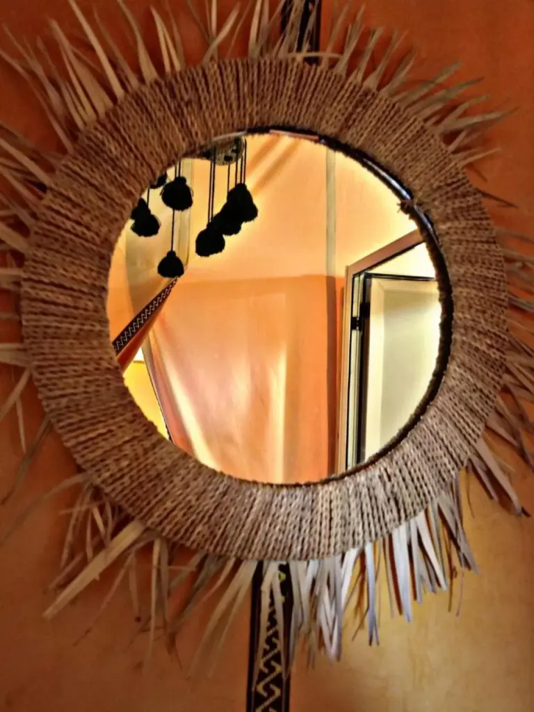 Round woven decorative mirror inside Zahra Luxury Desert Camp in Merzouga reflecting the tent interior and hanging lights.