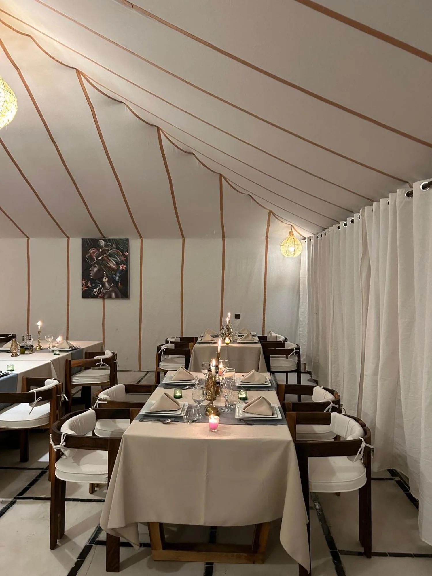 Elegant dining area inside Zahra Luxury Desert Camp in Merzouga with set tables, chairs, and warm ambient lighting.