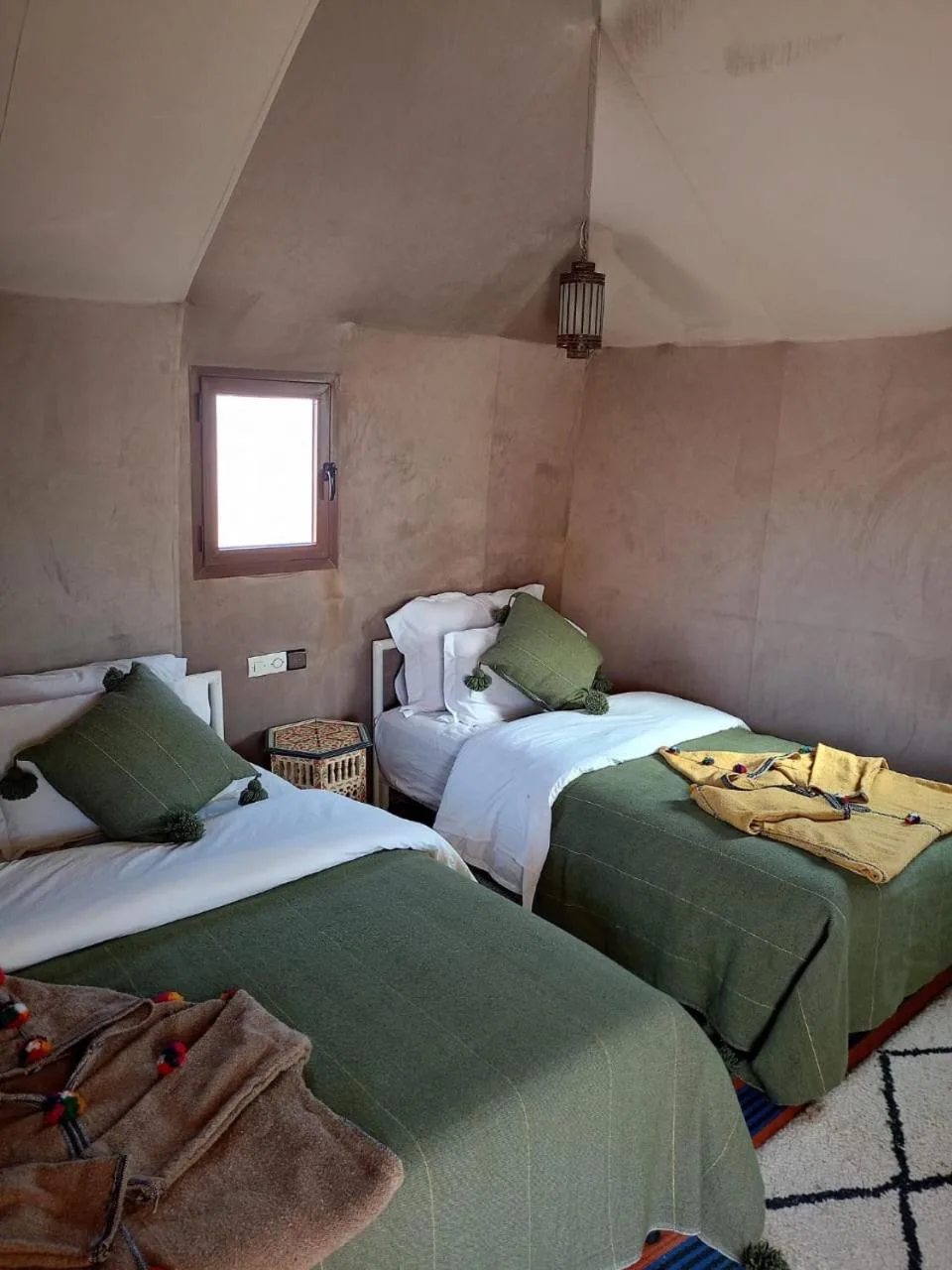 Double room inside Zahra Luxury Desert Camp in Merzouga with two green-accented beds and soft beige tent walls.