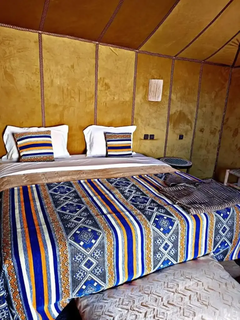 Double bed room at Zahra Luxury Desert Camp in Merzouga with colorful patterned bedding and golden tent walls.