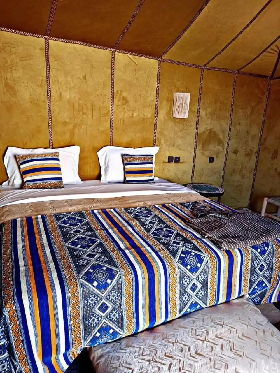 Double bed room at Zahra Luxury Desert Camp in Merzouga with colorful patterned bedding and golden tent walls.