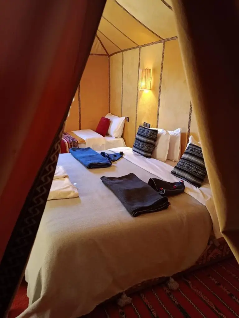Twin-bed tent room at Zahra Luxury Desert Camp in Merzouga with warm yellow walls, folded towels, and desert-style furnishings.