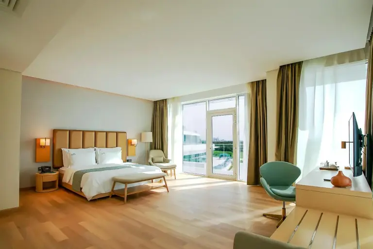 Bright guest room at Zoya Health & Wellbeing Resort in Ajman with a king bed, seating area, and balcony doors