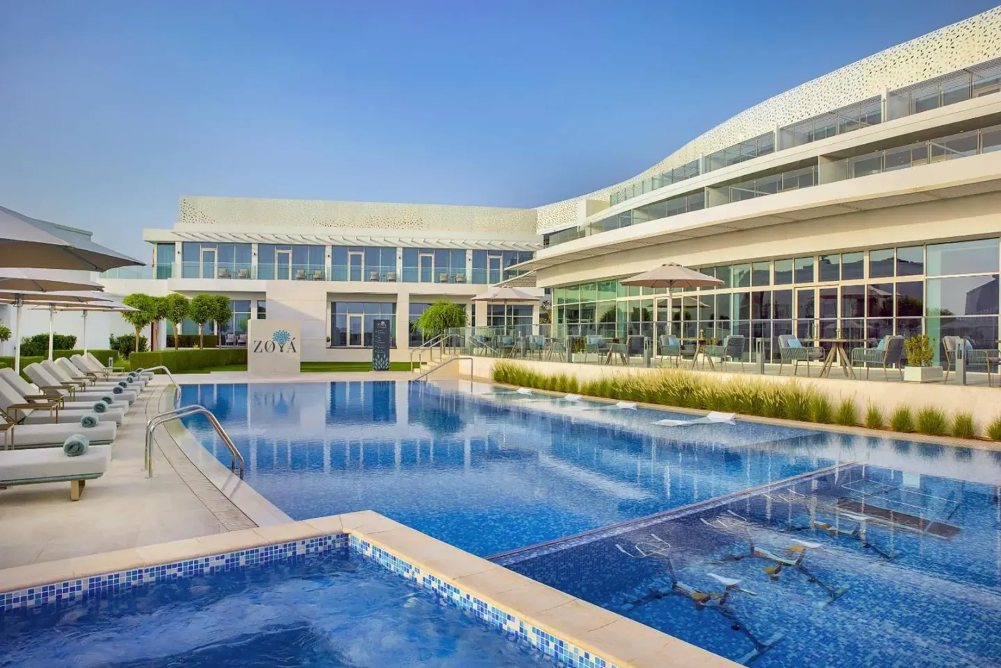 Outdoor pool area at Zoya Health & Wellbeing Resort in Ajman with loungers and resort building